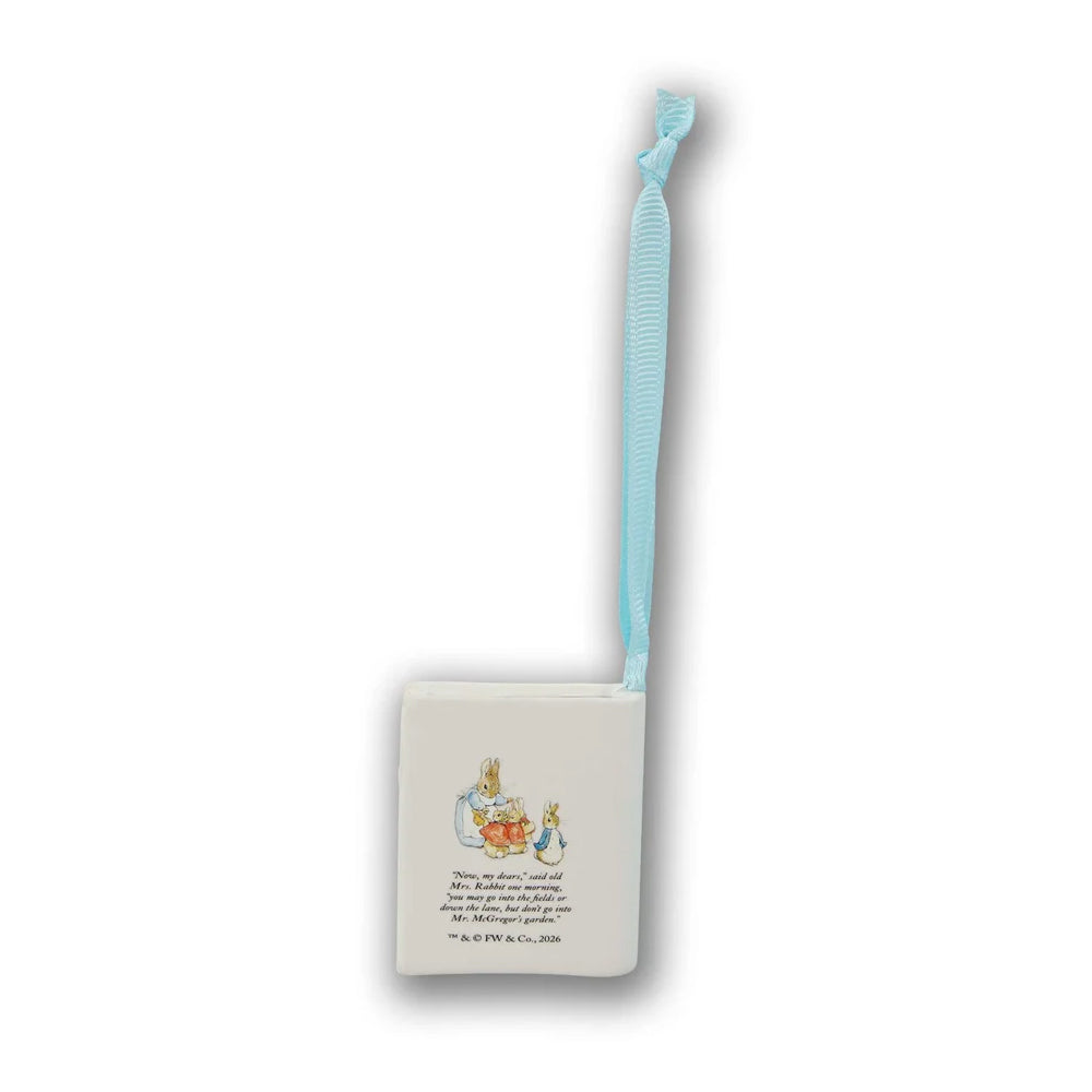 A square white Beatrix Potter-themed ornament featuring a small illustration of Peter Rabbit and the quote 'There is no greater pleasure in reading than the act of reading itself.' It has a light blue ribbon loop at the top, shown against a plain white background.