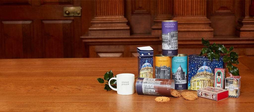 Packets and boxes of Bodleian food products are grouped together on a wooden table with a view of a wood clad room in the background