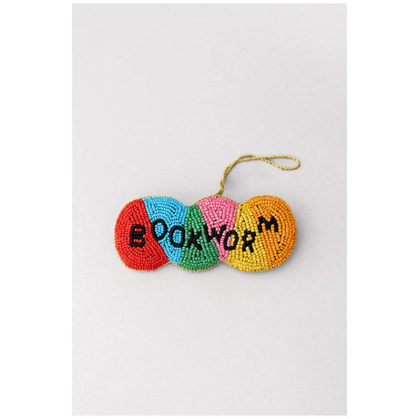 A colorful beaded ornament shaped like a worm with the word 'BOOKWORM' spelled out in black beads, hanging from a gold string on a light gray background.