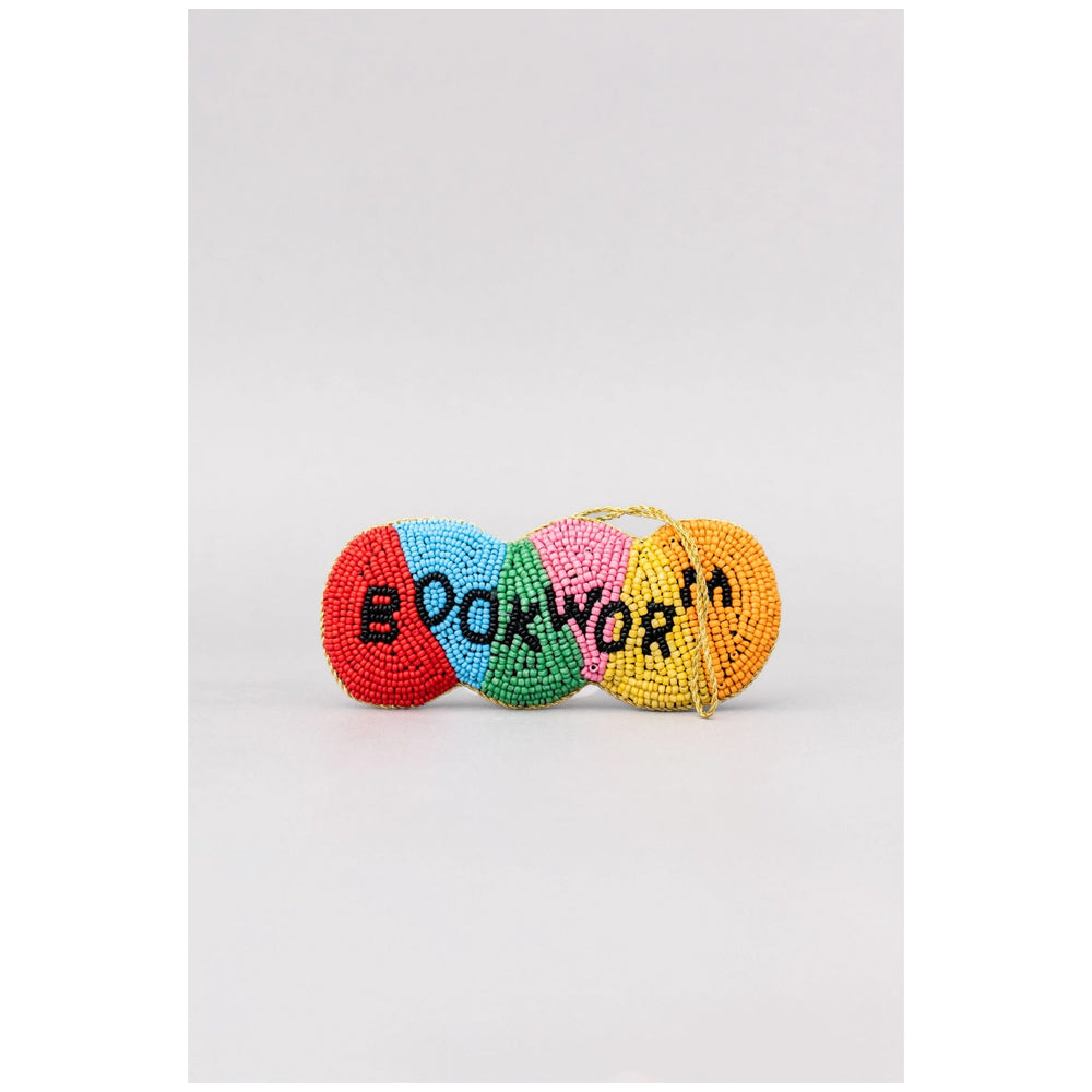 A small beaded accessory with four colorful segments in red, light blue, pink, and yellow, featuring the word 'BOOKWORM' in black beads, set against a plain light gray background.