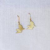 Gold bird-shaped earrings on a light gray fabric background