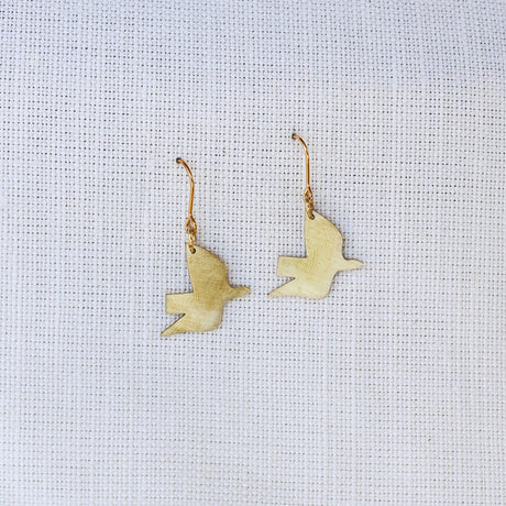 Gold bird-shaped earrings on a light gray fabric background