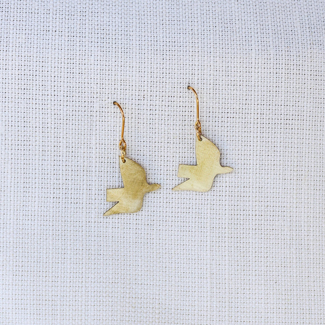 Gold bird-shaped earrings on a light gray fabric background