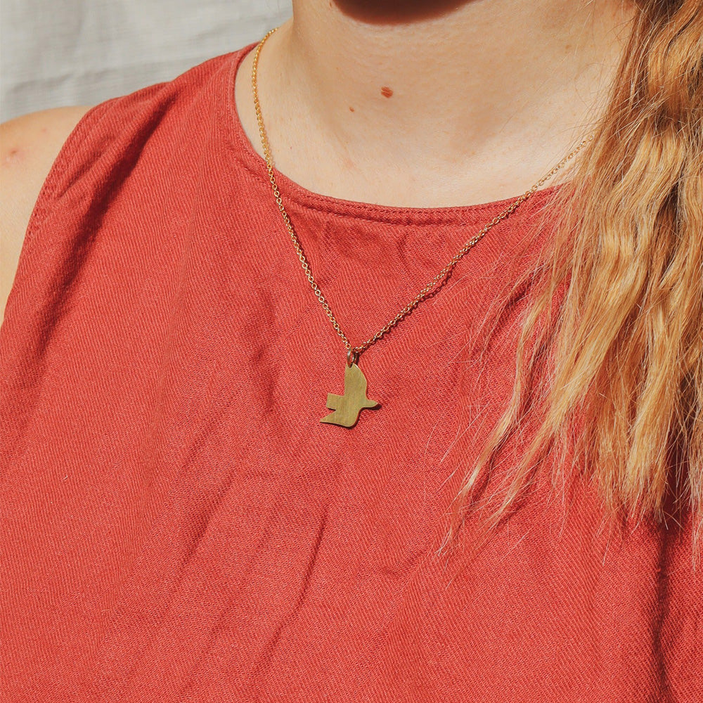Person wearing a gold necklace with a bird pendant on a red shirt.