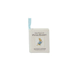 A square white book-shaped item featuring 'The Tale of Peter Rabbit' by Beatrix Potter, with a small light blue ribbon bookmark attached at the top and an illustration of Peter Rabbit on the front.