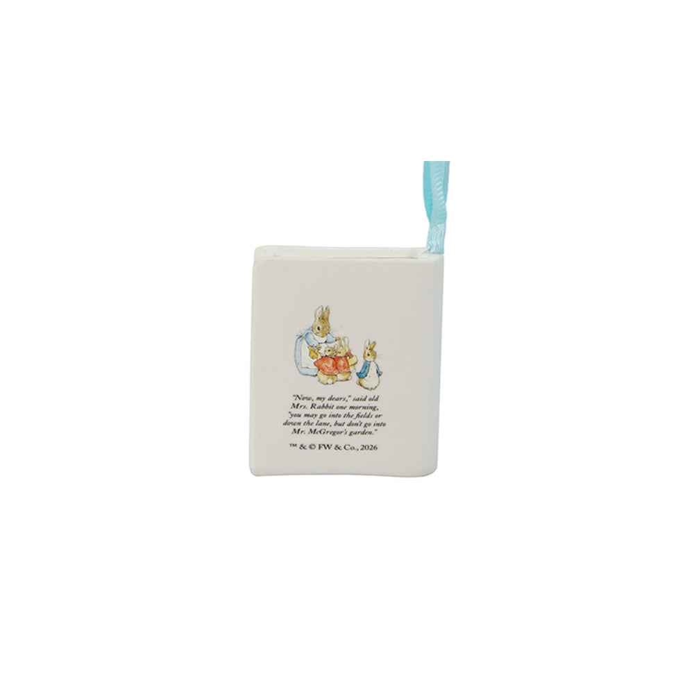 A square white ceramic ornament featuring a small illustration of Peter Rabbit and his mother with printed text, complete with a light blue ribbon loop at the top, shown on a plain white background.
