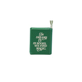 A small green book-shaped hanging decoration with white text reading 'In Dreams & In Books, We Find Magic.' on a plain white background.